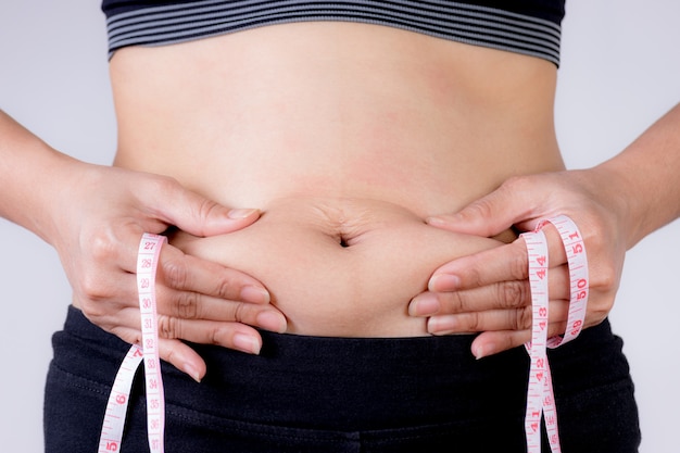 Mano de mujer gorda con exceso de grasa del vientre con cinta métrica. Reducir el concepto de vientre.