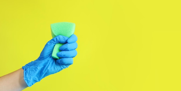La mano de una mujer en un guante azul aprieta una esponja para lavar los platos Limpieza de la casa