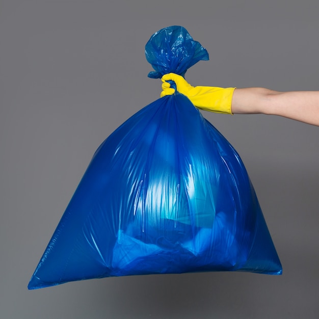 La mano de una mujer en un guante de goma sostiene una bolsa de plástico azul llena de basura.