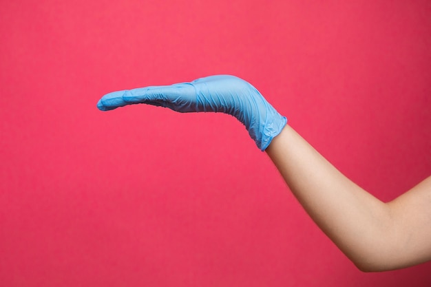 Mano de mujer en guante médico azul pretendiendo sostener medicina sobre fondo rosa