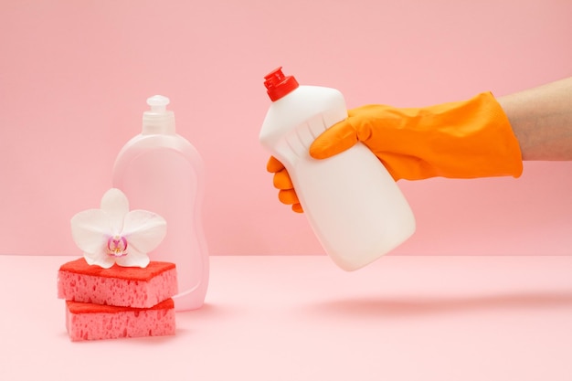 Mano de mujer en un guante protector de goma con una botella de líquido para lavar platos