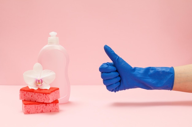 Mano de mujer en guante protector de goma con el pulgar hacia arriba Botella de esponjas líquidas para lavar platos