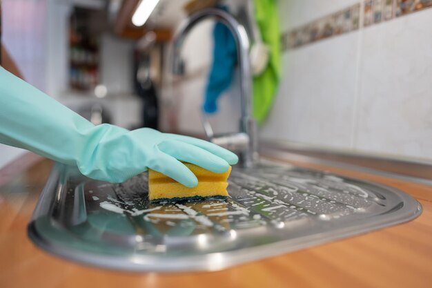 Mano de mujer con guantes fregando la cocina con estropajo y jabón