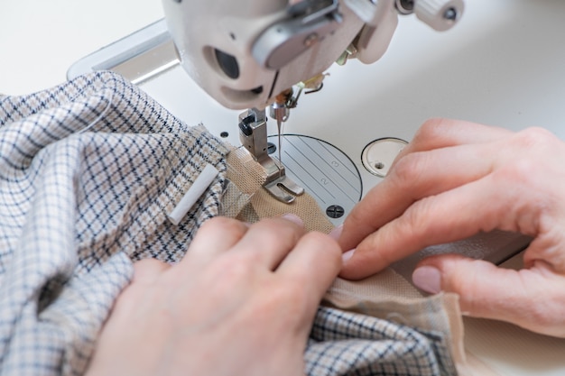 Mano de mujer guiando un paño blanco a través de una máquina de coser. Vista de primer plano.