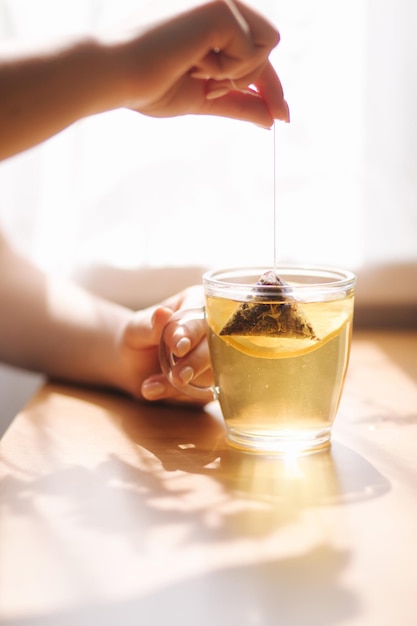 Mano de mujer haciendo té negro con limón en la mesa de madera