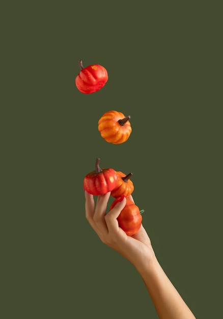 Mano de mujer hermosa haciendo malabares con calabazas sobre fondo verde oscuro Colores de otoño Concepto de Halloween