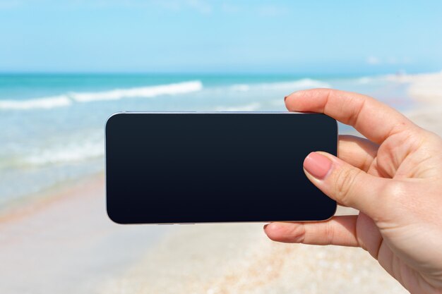 Mano de mujer hermosa con teléfono inteligente en la playa