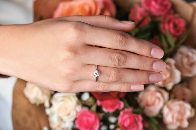 Mano de mujer con un hermoso anillo de compromiso en el dedo sobre un primer plano de flores