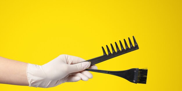 Mano de mujer con herramientas de peluquería y accesorios aislados en amarillo