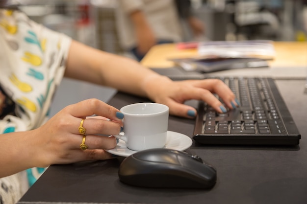 Mano de mujer holdding taza de café con el fondo de la mesa de trabajo