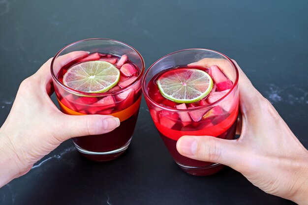 Mano de mujer y hombre sosteniendo una copa de sangría de vino tinto en mesa negra