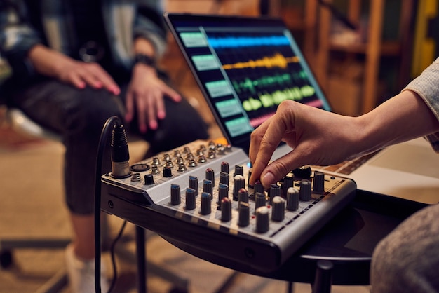 Foto mano de mujer joven ajustando el sonido mientras graba música en el estudio