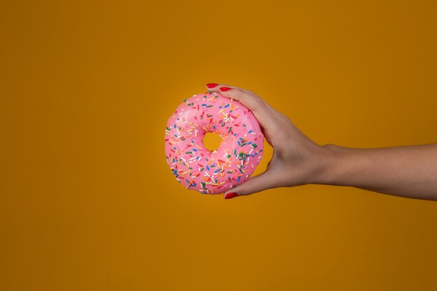 Mano de mujer joven caucásica sosteniendo una deliciosa dona de chocolate dulce sobre aislado