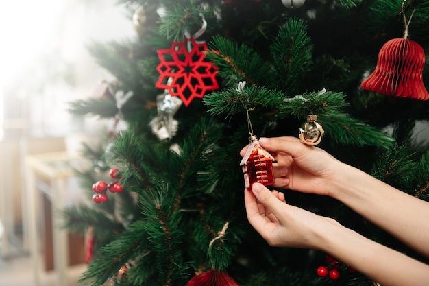 La mano de una mujer joven decorando el árbol de Navidad en el interior Celebración de año nuevoxAxA