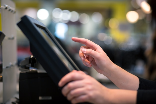 Mano de mujer joven haciendo pago de proceso en una caja registradora con pantalla táctil, concepto de finanzas