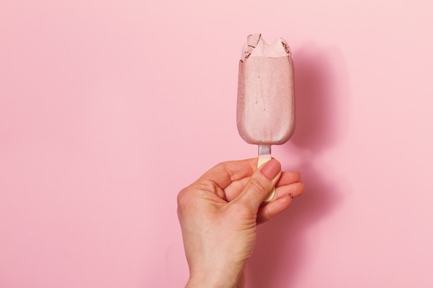 Mano de mujer joven con helado sobre fondo de color rosa. Fondo De La Moda. Concepto Del Verano.