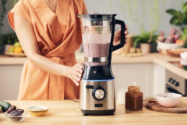 Mano de mujer joven preparando batido en licuadora