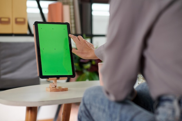 Mano de mujer joven que va a tocar la pantalla verde en blanco de la tableta en el soporte
