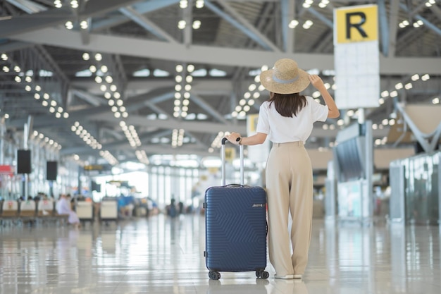 Mano de mujer joven sosteniendo el asa del equipaje antes de verificar el tiempo de vuelo en el aeropuerto Conceptos de viaje y vacaciones de seguro de transporte