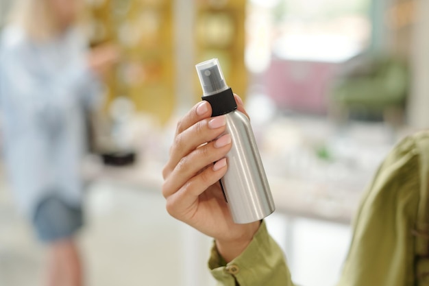 Mano de mujer joven sosteniendo una botella metálica que contiene un producto líquido para el cuidado del cabello