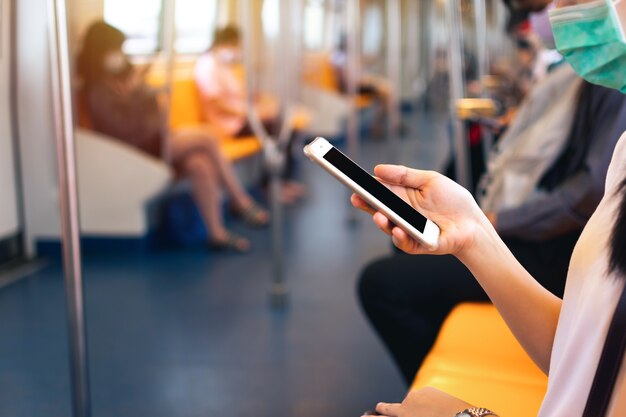 Mano de mujer joven sosteniendo y usando el teléfono móvil dentro del tren subterráneo con trazado de recorte en la pantalla