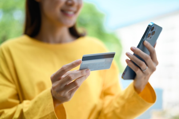 Mano de mujer joven con tarjeta de crédito y usando un teléfono inteligente para pagar en línea o revisar su cuenta bancaria