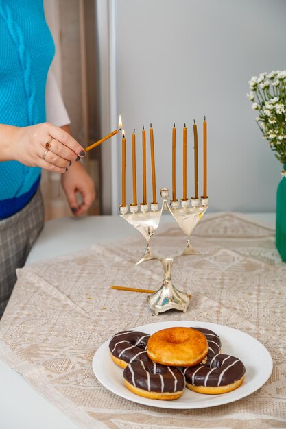 La mano de una mujer judía en la cocina del comedor enciende velas en Hanukkah sobre la mesa