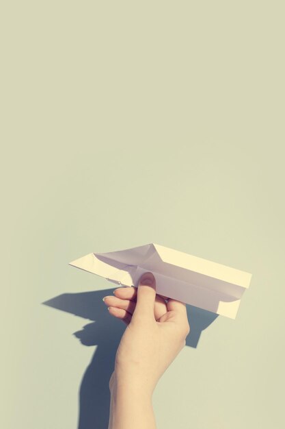 La mano de una mujer jugando con un avión de papel blanco