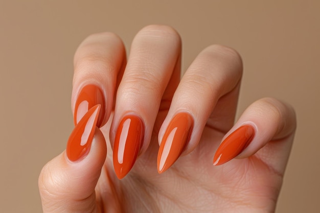 Una mano de mujer con largas uñas en forma de almendra pintadas con esmalte de uñas de color naranja brillante