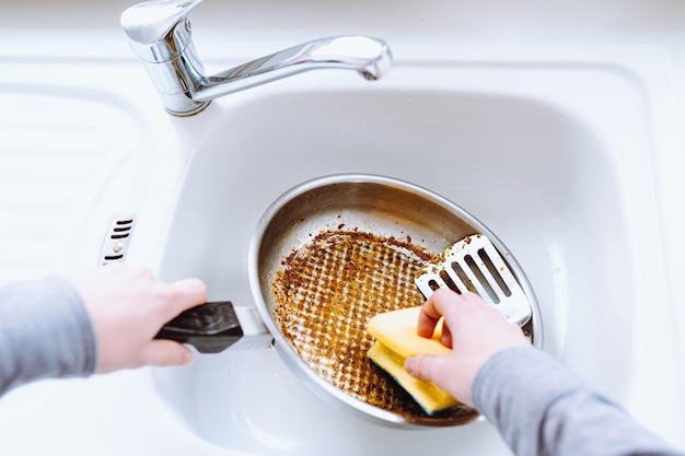 la mano de una mujer lava una sartén grasienta quemada con un paño de cocina en el fregadero