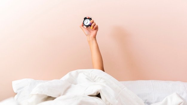 Foto mano de mujer levantando un reloj debajo de las sábanas