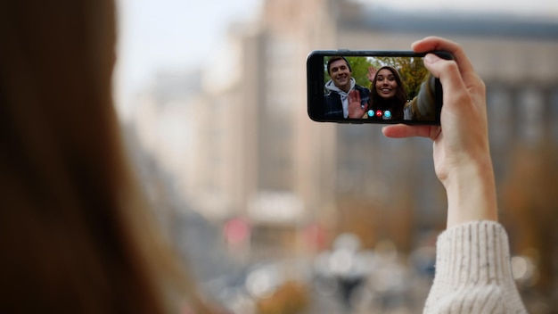 La mano de la mujer llamando por video a sus amigos de teléfono inteligente en primer plano una pareja feliz agitando la pantalla