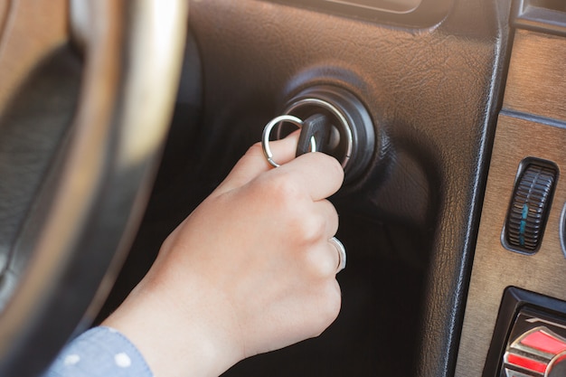 La mano de la mujer en la llave del coche, intenta arrancar el motor, encender la llave en el ojo de la cerradura, el panel automático y la rueda en el fondo. Llave insertada en la cerradura. Comienzo del viaje. Concepto de auto a partir