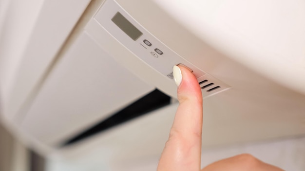 Foto mano de mujer con manicura ligera presiona el botón para encender el dispositivo de aire acondicionado para ajustar la temperatura en el primer plano de la premisa del apartamento