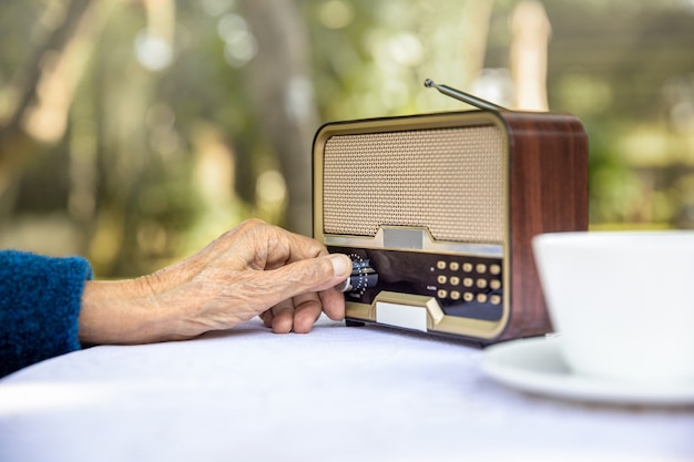 Foto mano de mujer mayor girando la perilla de radio vintage en el patio trasero.