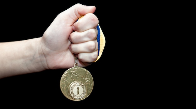 Mano de mujer con medalla de oro sobre fondo negro. Concepto de premio y victoria