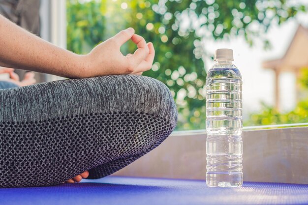 Mano de una mujer meditando en una pose de yoga sobre una alfombra para yoga y una botella de agua