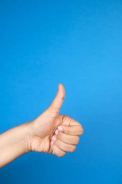 Foto mano de mujer mostrando un pulgar hacia arriba sobre fondo azul.