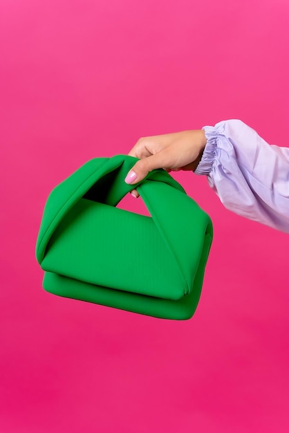 Mano de una mujer con muchos bolsos verdes en un estudio de moda de fondo rosa