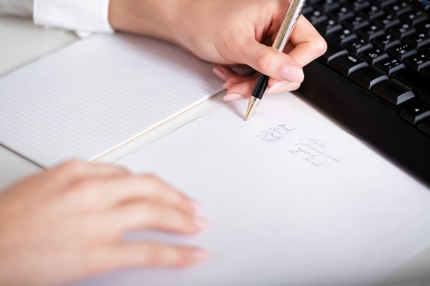Mano de mujer de negocios escribiendo en papel. mano y bloc de notas de cerca