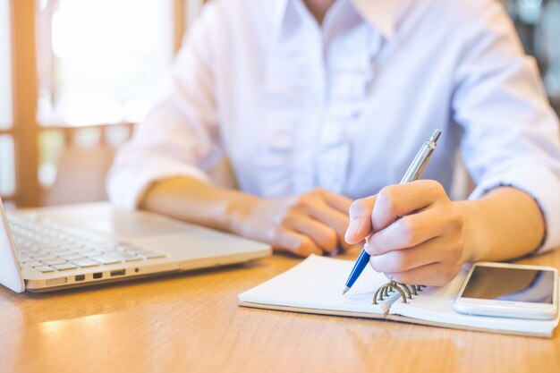 La mano de la mujer de negocios está escribiendo con una pluma en una libreta.