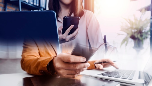 Mano de mujer de negocios trabajando con tableta de computadora portátil y teléfono inteligente en la oficina moderna con diagrama de icono virtual en la oficina moderna a la luz de la mañana