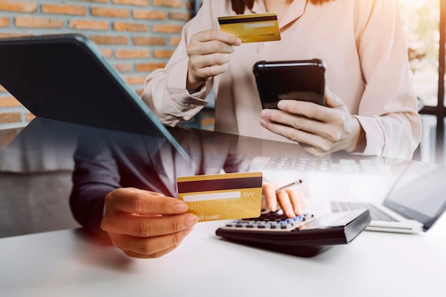 Mano de mujer de negocios usando pagos de tableta de teléfono inteligente y sosteniendo tarjeta de crédito compras en línea tableta digital omnicanal acoplando computadora de teclado en la oficina a la luz del sol