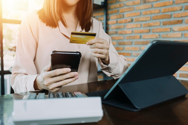 Mano de mujer de negocios usando pagos de tableta de teléfono inteligente y sosteniendo tarjeta de crédito compras en línea tableta digital omnicanal acoplando computadora de teclado en la oficina a la luz del sol