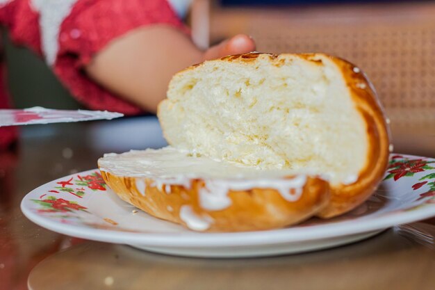 la mano de la mujer panadero extendiendo mayonesa en un pan abierto con un cuchillo en un plato en una mesa de desayuno