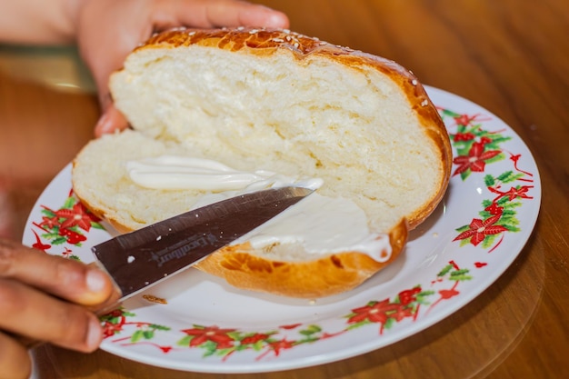 Foto la mano de la mujer panadero extendiendo mayonesa en un pan abierto con un cuchillo en un plato en una mesa de desayuno