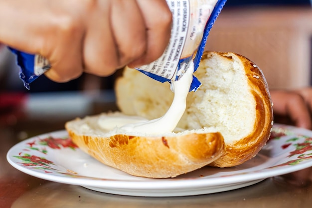 Foto la mano de la mujer panadero extendiendo mayonesa en un pan abierto en un plato en una mesa de desayuno