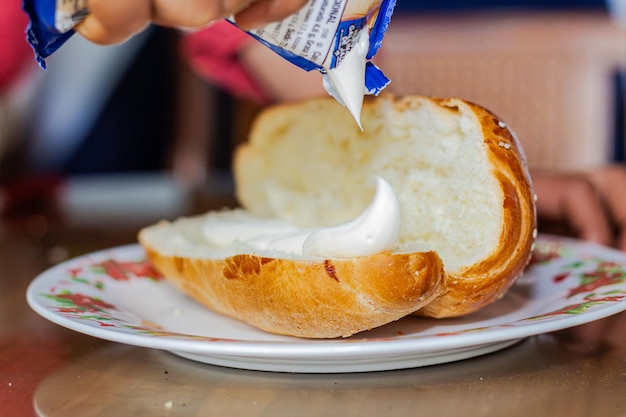 La mano de la mujer panadero extendiendo mayonesa en un pan abierto en un plato en una mesa de desayuno