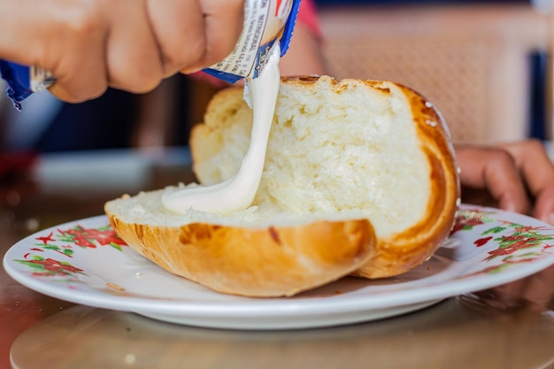 La mano de la mujer panadero extendiendo mayonesa en un pan abierto en un plato en una mesa de desayuno