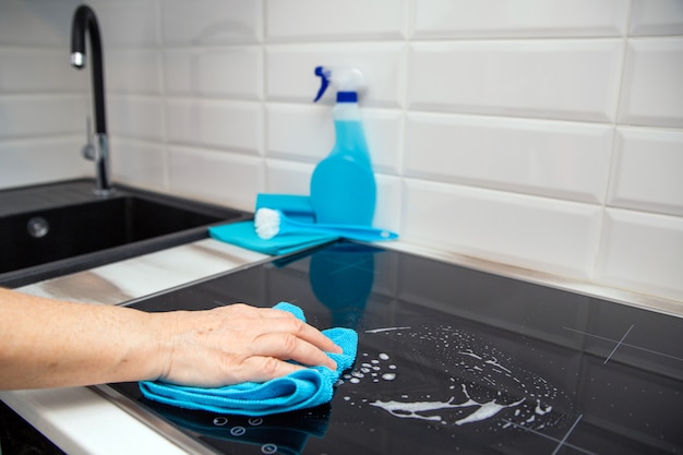 La mano de una mujer con un paño azul de microfibra frota un plato de vitrocerámica en la cocina.